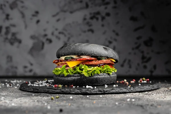 Homemade big burger with a black bun on rustic black background. fast food and junk food concept.
