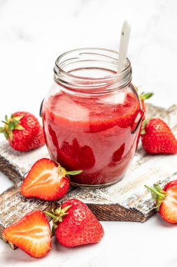 Cam kavanozda çilek reçeli ve beyaz masada bir kaşık. dikey görüntü. en üstteki görünüm,