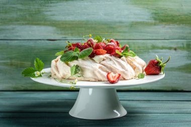 Ev yapımı lezzetli kremalı Pavlova kremalı, taze çilekli ve ahşap arka planda naneli, yazı için yer, üst manzara..