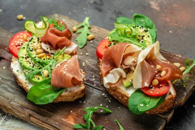 Krem peynirli sandviç, jambon, avokado ve ahşap arka planda taze yeşillikler. Keto kahvaltı ya da aperatif, üst manzara.