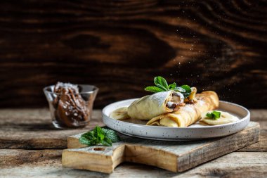 Çikolata kaplı krepler ve beyaz tabakta muz. İnce krep, blini. Lezzetli kahvaltı ya da atıştırmalık. Yemek tarifi geçmişi. Kapat..