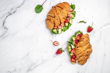 Avokado, çilekli, peynirli, peynirli kruvasan sandviçi susam ve kimyon serpiştirilmiş taze salata lezzetli kahvaltı veya atıştırmalık Keto diyet vejetaryen yemeği..