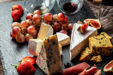 Çeşitli peynir çeşitleri, geleneksel Fransız parçaları, İtalyan ve İspanyol manchego peyniri üzümlü ve incirli ahşap masada servis edilmiş..