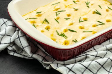 Pişirme kabında çiğ Focaccia hamuru. Siyah arka planda biberiyeli geleneksel İtalyan Focaccia 'sı. afiş, menü, metin için tarif yeri, üst görünüm.