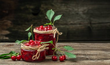 Bir kavanoz kiraz reçeli ve ekşi kiraz. Şerbetli kiraz. Olgun kirazlar. Tatlı kırmızı kirazlar. Ahşap bir arka planda konserve meyve.