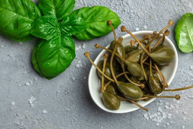 Kapari. Salamura edilmiş ya da turşulu kapari meyvesi. Küçük bir kasede taze biberiye, gri arka planda. metin için yer, üst görünüm.