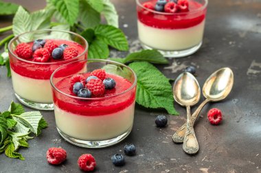 Ahudududulu panna cotta, üzerinde ahududu reçeli ve koyu bir arka plan. Küçük kavanozlarda krema soslu böğürtlen tatlısı. metin için yer.