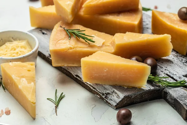 Parmesan cheese on a wooden board, Hard cheese, olives, rosemary on a light background. place for text, top view.