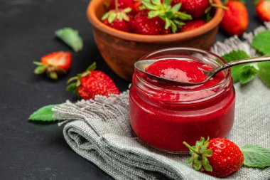 Cam kavanozda çilek reçeli ve karanlık masa kaşığı. en üstteki görünüm,