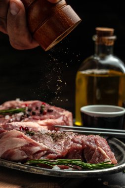 Şef çiğ bifteğe biber döker. Sahne arkasında ızgara domuz eti hazırlıyorum. Mutfak, yemek pişirme konsepti. dikey görüntü. metin için yer.