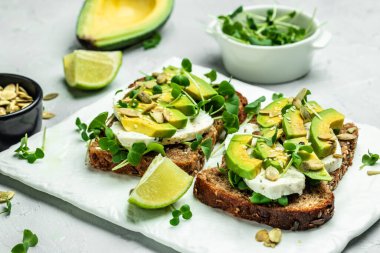 Sağlıklı avokado tostları, çavdar ekmeği dilimlenmiş avokado, peynir, balkabağı, fındık ve susamlı kahvaltı ya da öğle yemeği. Vejetaryen yemeği. Vejetaryen menüsü. Yemek tarifi.