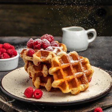 Süt sürahisi ile servis edilen bir toz bulutunun dondurucu hareketinde şekerli ahududulu Belçika waffleları. Lezzetli kahvaltı ya da atıştırmalık.