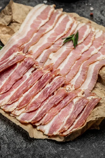 Close up Bacon slices. Pig meat. Pork belly with rosemary on a wooden board, Keto diet food ingredients. Restaurant menu, dieting, cookbook recipe.
