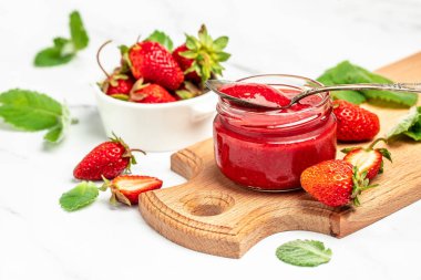 Cam kavanozda çilek reçeli ve beyaz masada bir kaşık. en üstteki görünüm,