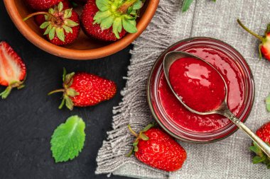 Cam kavanozda çilek reçeli ve karanlık masa kaşığı. en üstteki görünüm,