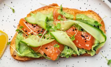 Krem peynirli sandviç, somon, avokado, salatalık, domates ve açık arkaplanda yeşillikler. Keto kahvaltısı ya da brunch. afiş, menü, metin için tarif yeri, üst görünüm.