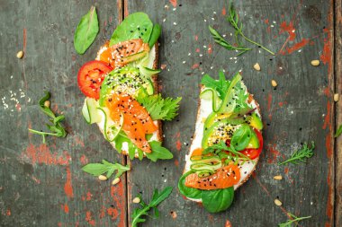 Krem peynirli sandviç, somon, avokado, salatalık, domates ve ahşap arka planda yeşillikler. Keto kahvaltısı ya da brunch. afiş, menü, metin için tarif yeri, üst görünüm.