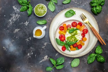Burrata peynirli salata, vişneli domates ve koyu arkaplanda yeşil pesto. Restoran menüsü, diyet, yemek kitabı tarifi üst görünümü.