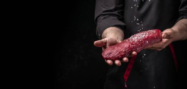 Biberiye ve baharatlı dondurulmuş biftekli şef tuzu. Karanlık bir arka planda taze et ya da domuz eti hazırlıyorum. Uzun pankart biçimi.