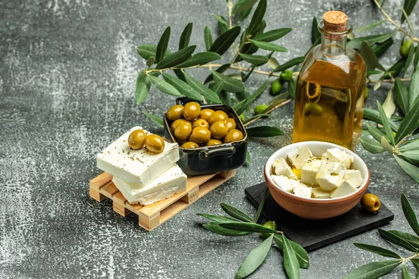 Feta cheese with olives and green herbs and olive oil sauce in bowl on dark background. place for text, top view.