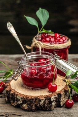 Ahşap arka planda taze kırmızı kiraz meyvesi. Bir kavanoz kiraz reçeli ve ekşi kiraz. Şerbetli kiraz. Konserve meyve. dikey görüntü. Üst Manzara. metin için yer.