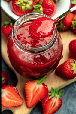 Cam kavanozda çilek reçeli ve masada kaşık. dikey görüntü. en üstteki görünüm.