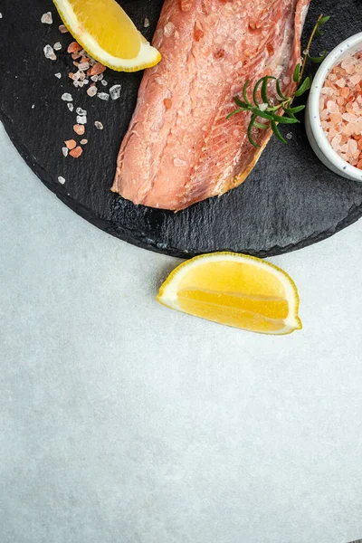 salmon fillet with rosemary and salt on light board. Pescetarian seafood for cooking. fish fillet with cooking ingredients, herbs and lemon. top view.