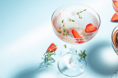 Ayyaş Tazeleyici Gül Şarabı, çilekli kokteyl veya moktail, tazeleyici yaz içeceği şampanya, çilek, buz küpleri ve mavi arka planda biberiye,