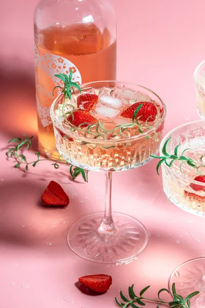 drink cocktail with ice in a glass on pink background. refreshing fruit cocktail or punch with wine champagne, strawberries, ice and rosemary.