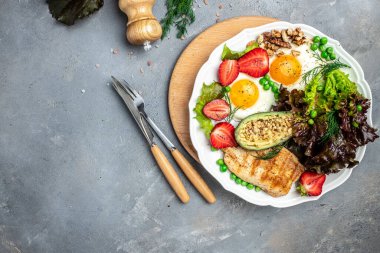 Ketogenic breakfast. Keto low carb Fried eggs, avocado, grilled chicken fillet, nuts, strawberries and fresh salad on a gray background. keto diet. Long banner format. top view.