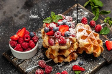 Ahududu, çilek ve yaban mersinli Belçika waffleları, siyah arkaplanda şeker tozu.