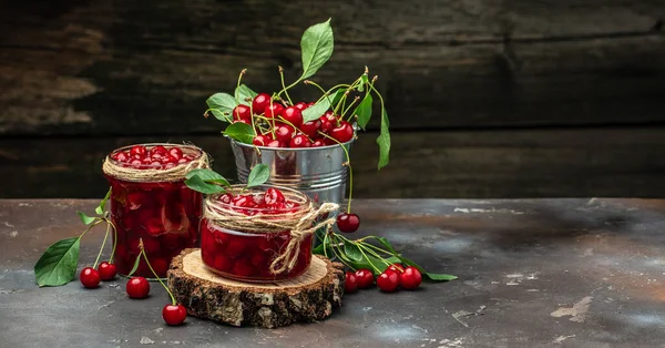 Fresh red cherries fruit on wooden background. Jar of cherry jam and sour cherries. Berries cherry with syrup. Canned fruit. Long banner format. place for text.