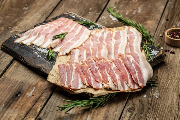 Bacon slices. Pig meat. Pork belly with rosemary on a wooden board, Keto diet food ingredients. Restaurant menu, dieting, cookbook recipe top view.