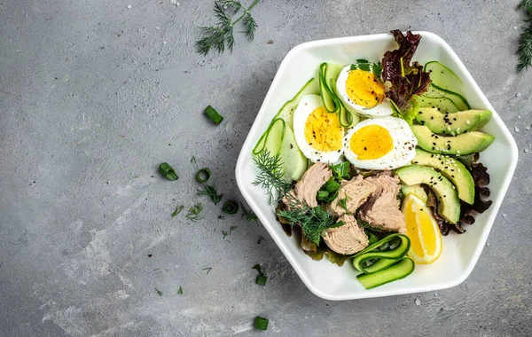 Ketogenic low carbs diet, Plate with keto foods: two eggs, avocado, tuna, cucumber and fresh salad. Healthy fats, clean eating for weight loss. top view.