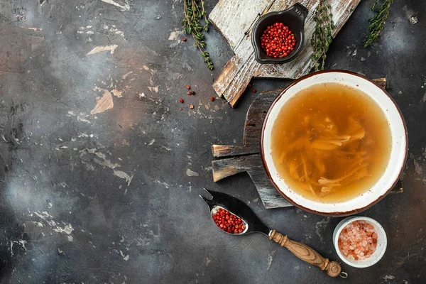 clear broth with pieces of farm organic meat on bone on a dark background, banner, menu, recipe place for text, top view.