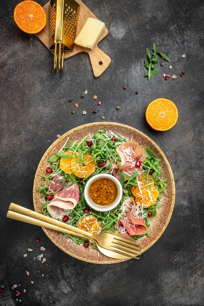 winter salad with arugula mandarins, prosciutto jamon and Parmesan cheese. place for text, top view.
