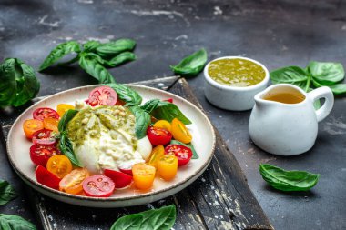 Burrata cheese with tomatoes and green pesto. Vegetarian italian food. Food recipe background. Close up.