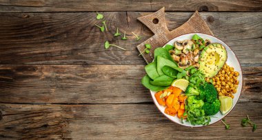 vegetable vegetarian buddha bowl avocado, mushrooms, broccoli, spinach, chickpeas, pumpkin on a wooden background. Long banner format. top view.