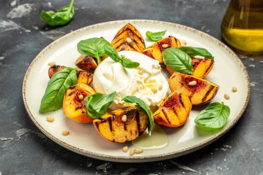 Burrata soft cheese and grilled peaches with basil and pine nuts, drizzled honey, Food recipe background. Close up,