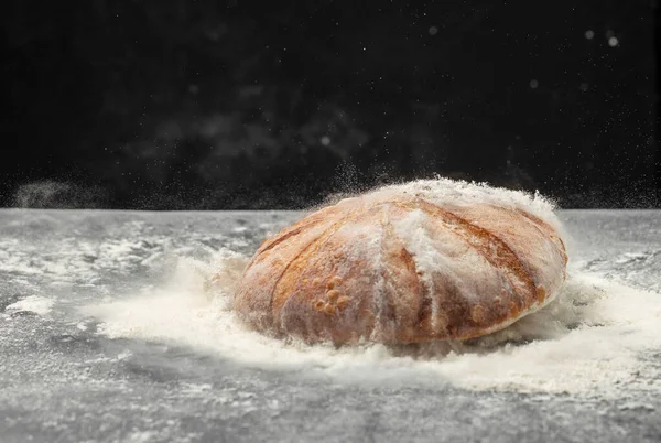 Homemade sourdough bread with powder in a freeze motion of a cloud of powder midair. Culinary, cooking, bakery concept.
