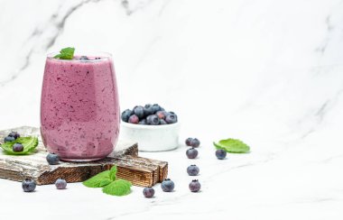 Böğürtlenli yoğurt, bardakta taze yaban mersini, nane yaprağı ve beyaz arka planda çiğ bira. Restoran menüsü, diyet, yemek kitabı tarifi üst görünümü.