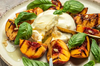 Burrata soft cheese and grilled peaches with basil and pine nuts, drizzled honey, Food recipe background. Close up,