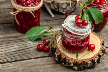Bir kavanoz kiraz reçeli ve ekşi kiraz. Şerbetli kiraz. Olgun kirazlar. Tatlı kırmızı kirazlar. Ahşap bir arka planda konserve meyve.