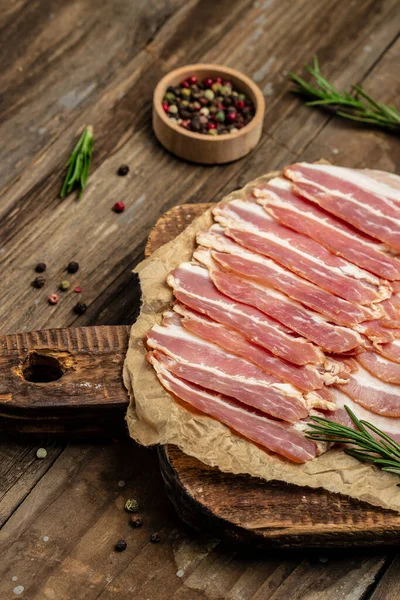 Close up Bacon slices. Pig meat. Pork belly with rosemary on a wooden board, Keto diet food ingredients. Restaurant menu, dieting, cookbook recipe.