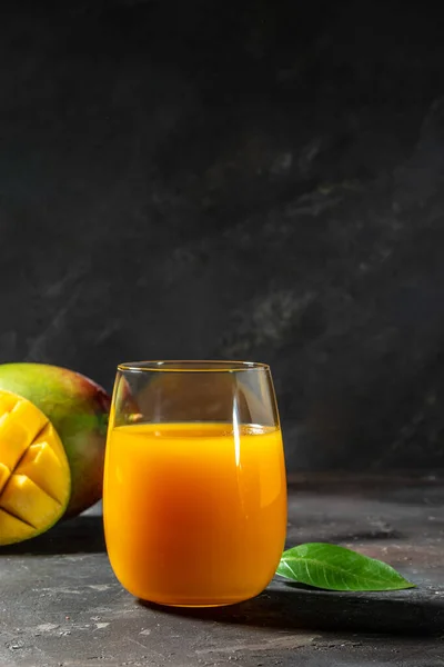 mango juice with Fresh tropical fruit on a dark background. vertical image. place for text.