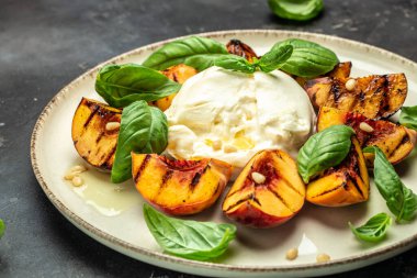 Burrata soft cheese and grilled peaches with basil and pine nuts, drizzled honey, Food recipe background. Close up,