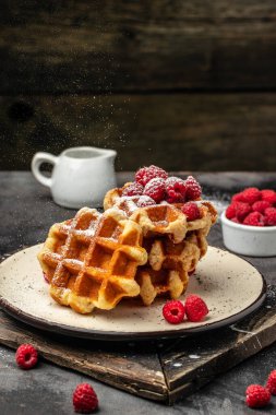 Süt sürahisi ile servis edilen bir toz bulutunun dondurucu hareketinde şekerli ahududulu Belçika waffleları. Lezzetli kahvaltı ya da atıştırmalık.