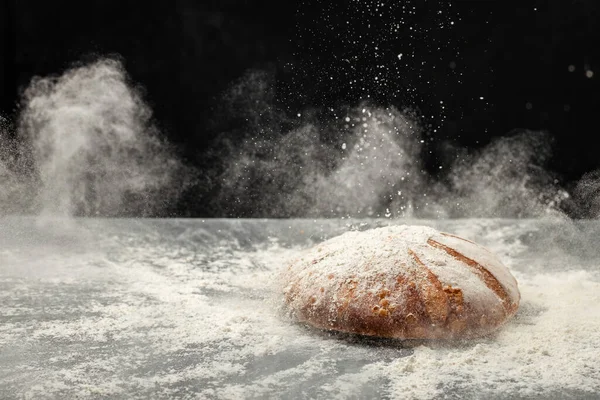 Fresh bread on table with powder in a freeze motion of a cloud of powder midair. Culinary, cooking, bakery concept.