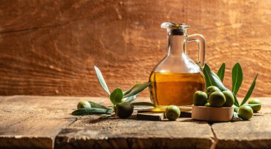 Glass container with olive oil branches and olives on a wooden background. Long banner format.