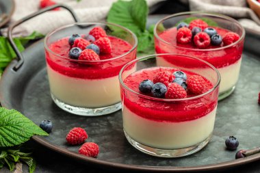 Ahudududulu panna cotta, üzerinde ahududu reçeli ve koyu bir arka plan. Küçük kavanozlarda krema soslu böğürtlen tatlısı. metin için yer.